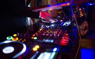 DJ at a mixer using DJ Equipment with colorful lights in the background.