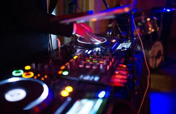DJ at a mixer using DJ Equipment with colorful lights in the background.